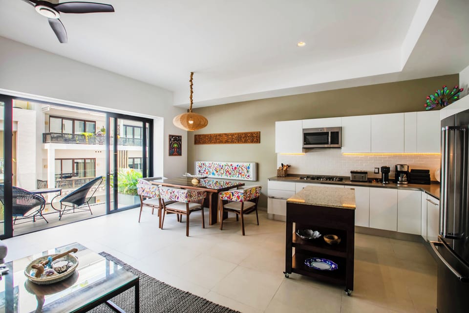 Bright, open-concept kitchen flows into the dining area with warm wood tones and colorful cushions. Sunlight streams through sliding doors to your private balcony, perfect for cooking, dining, and relaxing.