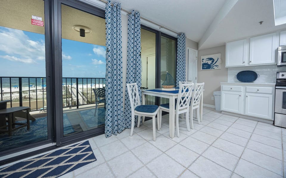 This dining area features a bright table set against vibrant blue curtains, with a lovely view of the beach just outside