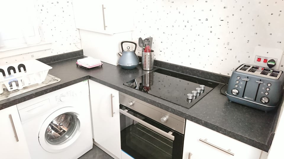 Kitchen with washing machine, kettle, 4 slice toaster and utensils.