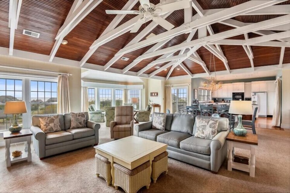 Relax in your light-filled living space, where soaring wood-beamed ceilings and panoramic windows frame stunning views. Sink into plush sofas as gentle breezes and natural beauty surround you.