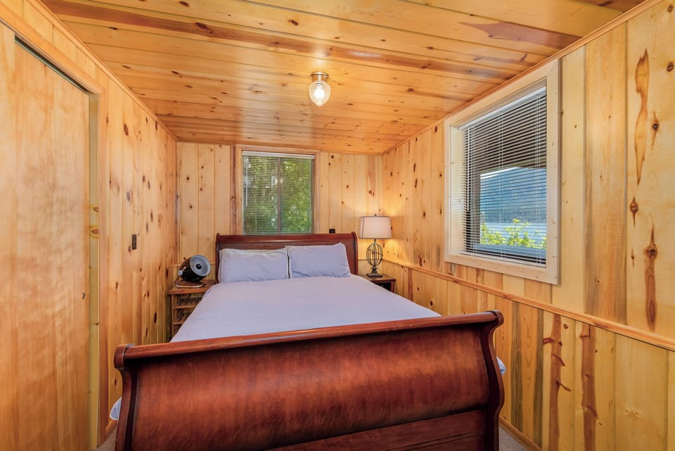 Queen bed nestled in a warm knotty‑pine bedroom with gentle natural light