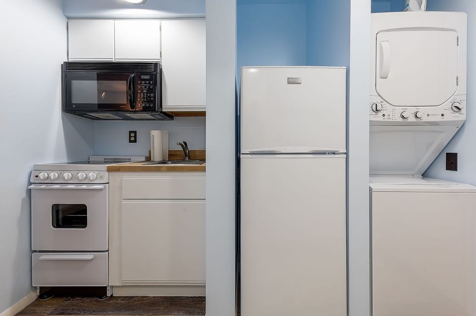A petite kitchenette featuring a microwave, refrigerator, and a washer & dryer.