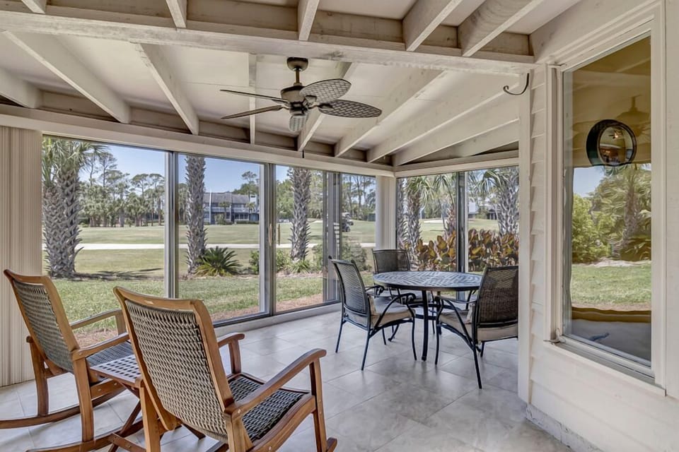 - Enjoy serene mornings or sunset dinners on this screened patio overlooking palms and greenery
- Rocking chairs and a ceiling fan create a breezy space for coffee or cards
- Spacious layout blends comfort and nature for all season relaxation