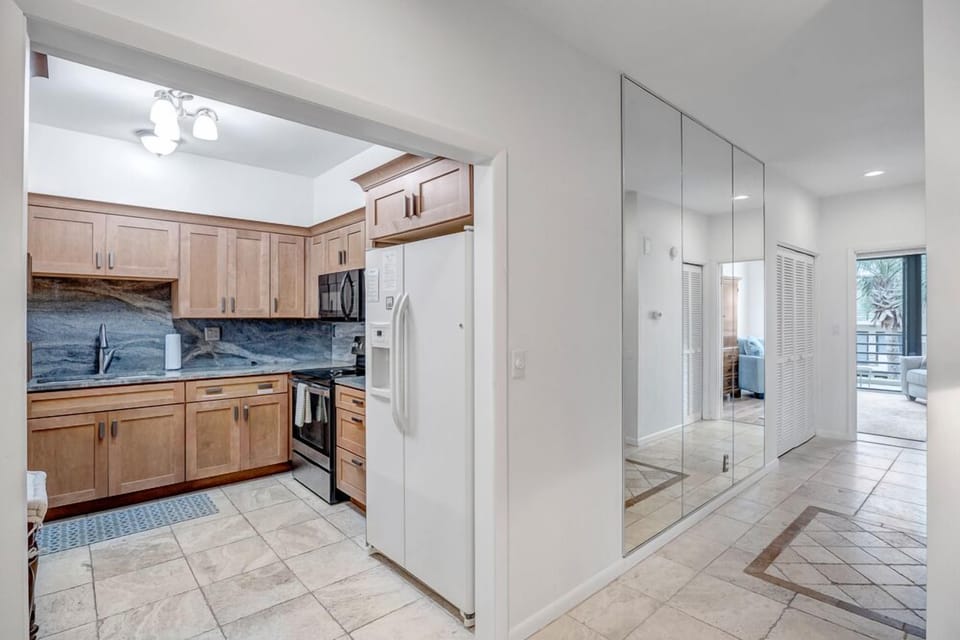 - Kitchen features wood cabinets, granite backsplash, and modern appliances
- Mirrored wall reflects natural light and creates a bright, open hallway feel
- Easy access to dining, living room, and outdoor areas from this central space