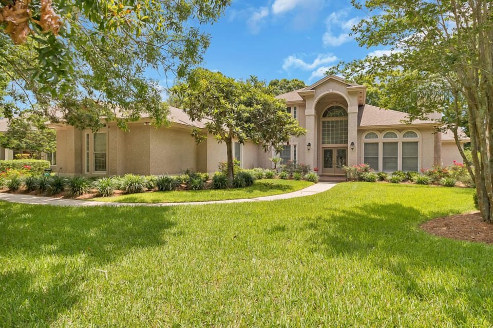 Elegant home with soaring entry windows, manicured landscaping, and a peaceful green lawn.