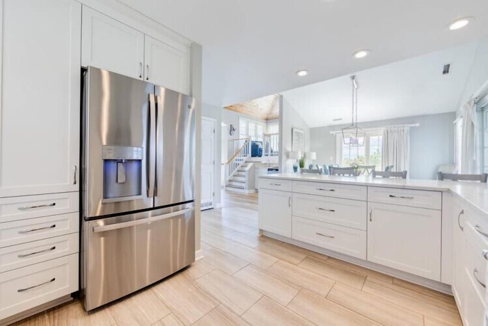 Step into your bright, open kitchen with sleek white cabinetry, stainless steel appliances, and elegant tile floors that flow into the inviting living spaces beyond.