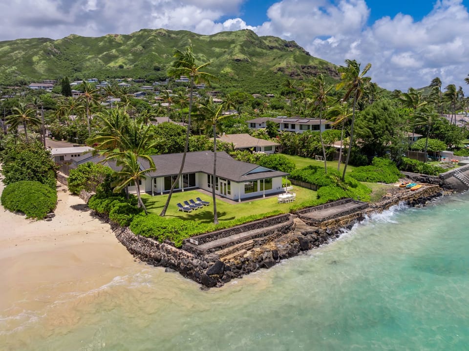 A beachfront Hawaiian retreat nestled between mountains and turquoise waters, offering privacy, lush tropical landscaping, and direct access to sandy shores in an idyllic island neighborhood.