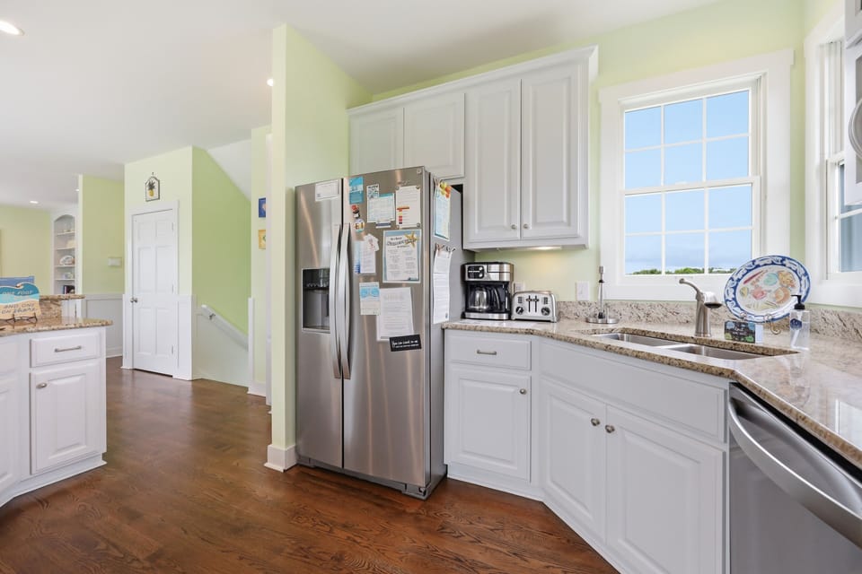 Bright, fully equipped kitchen with granite counters, stainless appliances, and coffee station ready for your morning brew. Large windows flood the space with natural light.