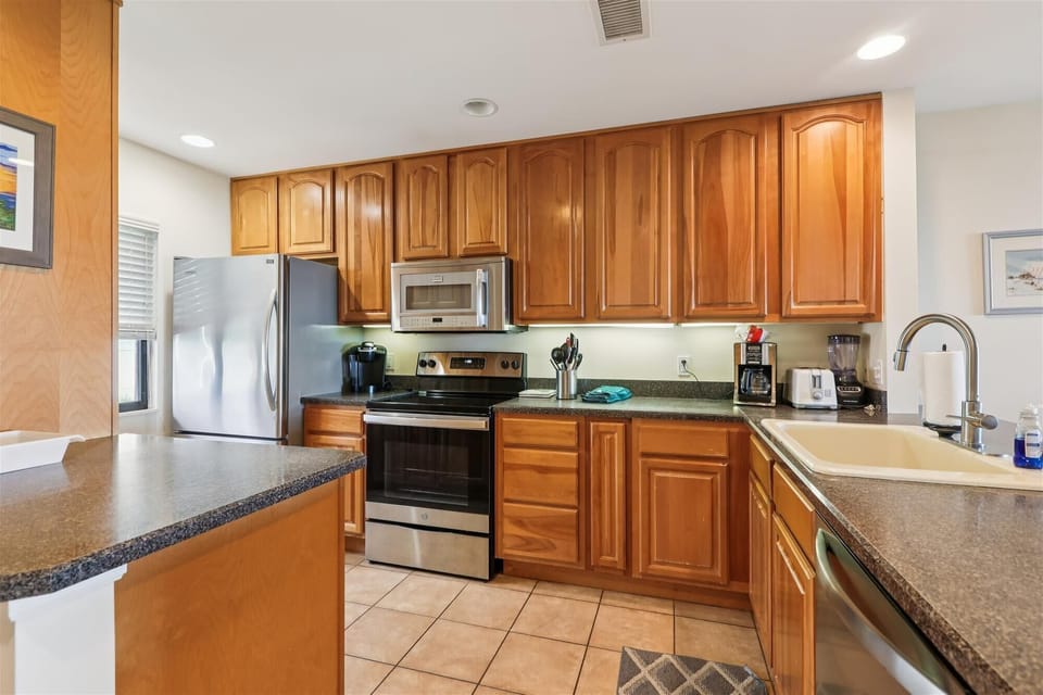 - Modern kitchen with wood cabinetry and tile flooring
- Fully equipped with stove, fridge, microwave, and sink
- Spacious counters for easy meal prep and cooking
