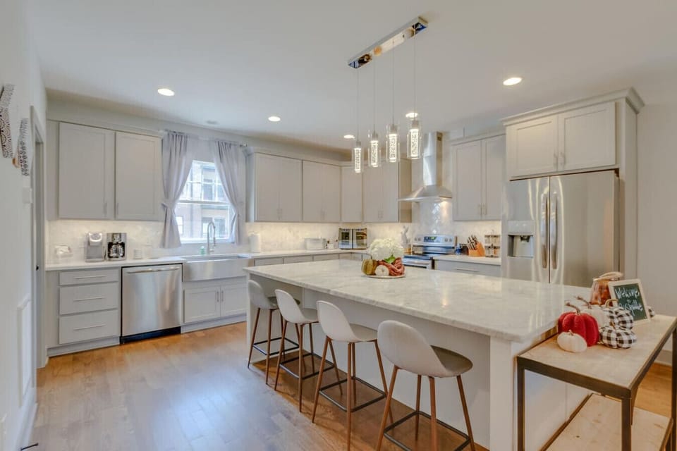 Kitchen with white cabinetry, marble island with bar stools, pendant lights, and stainless appliances