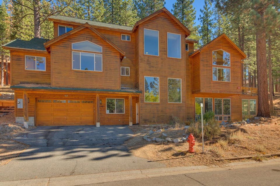 Three-story home with attached two-car garage and large windows, set among tall pines.
