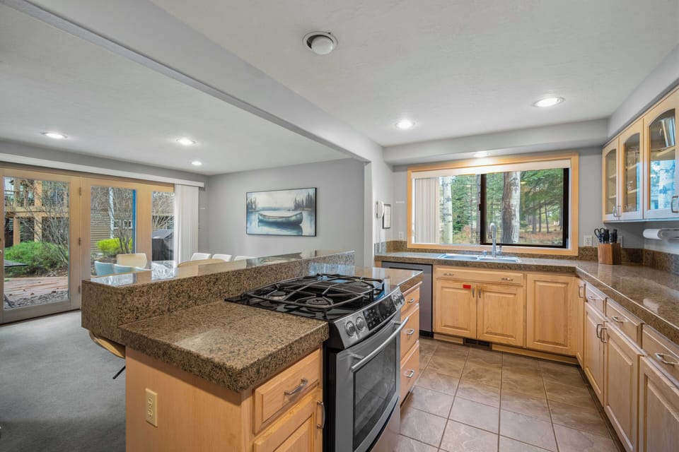 Your spacious kitchen features granite countertops, stainless steel appliances, and warm wood cabinetry with lovely forest views from the window.