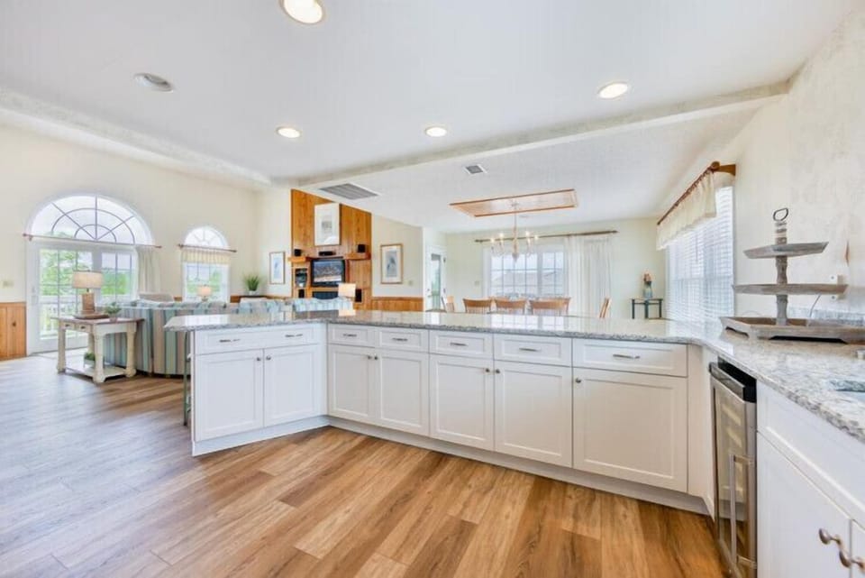 Spacious open-concept living where gleaming granite counters, white cabinetry, and warm wood floors invite you to gather, cook, and relax—all bathed in natural light from the arched windows overlooking the outdoors.