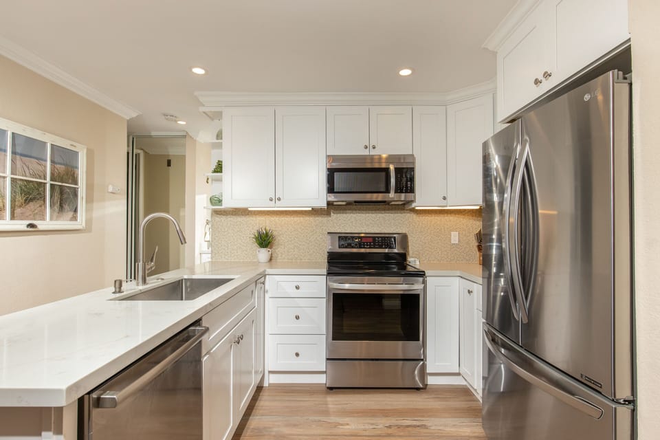 The chef's kitchen has a glass tile backsplash, new cabinets, electric kettle, and stainless appliances and sink.
