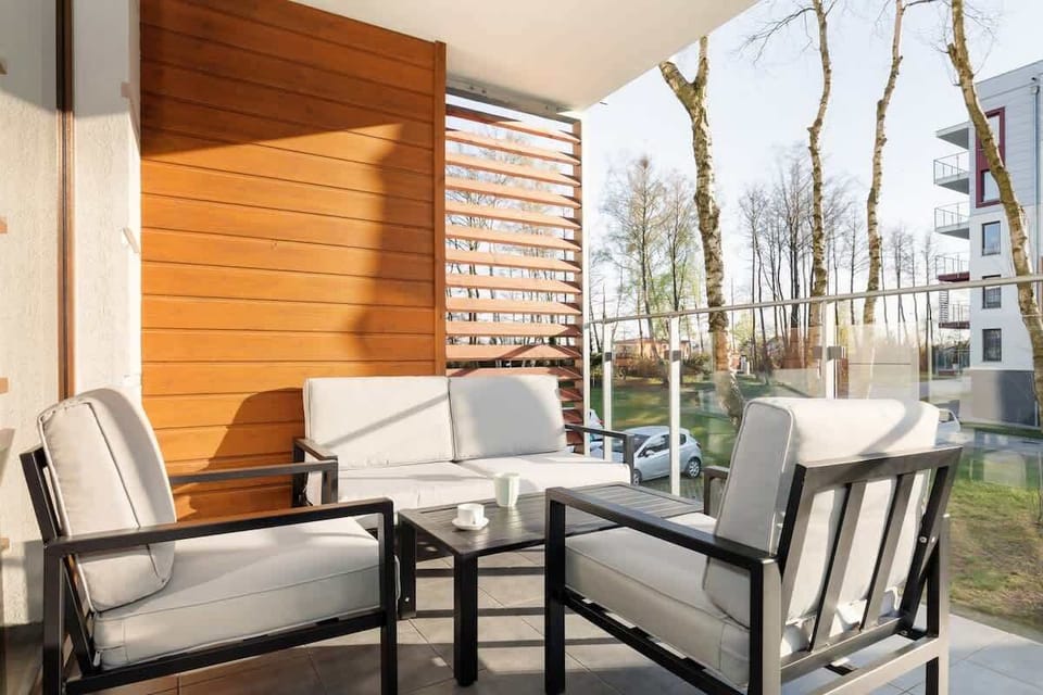 A cozy patio area with chairs and a table, surrounded by greenery and natural light.