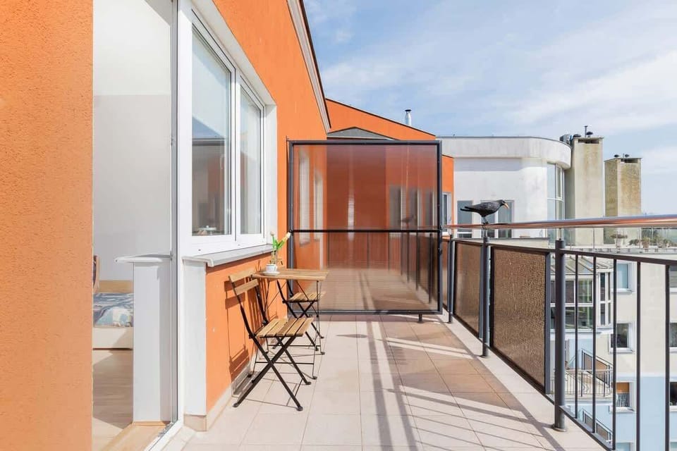 A cozy outdoor balcony with a table and chairs, framed by orange walls for a pop of color.