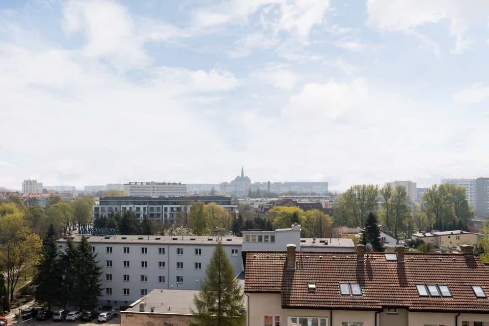 A scenic view of the city from the balcony, showing nearby rooftops and greenery in the distance.