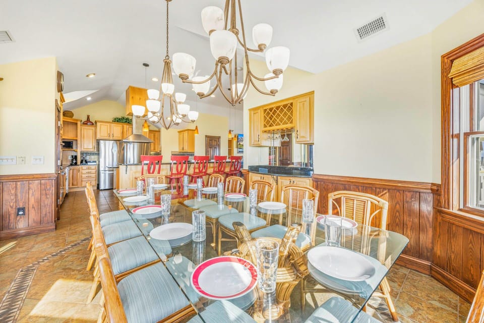 Gather around this elegant glass dining table where memorable meals unfold beneath warm chandeliers, connecting your group to the spacious gourmet kitchen.