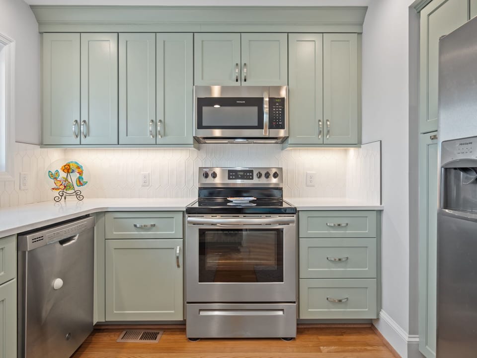 Step into your fully-equipped kitchen with sage-green cabinets, stainless steel appliances, and charming details that make cooking feel like home.
