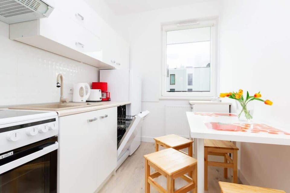 A well-equipped kitchen with white cabinets, a stovetop, and a dishwasher. A small dining table with two chairs sits by the window, adding a cozy touch.