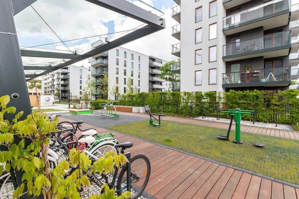 A view of the outdoor area near the building, featuring a walkway, bicycle parking, and lush landscaping.