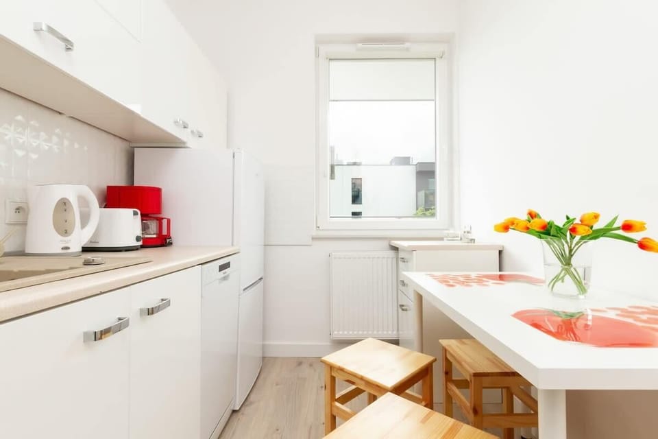 A well-equipped kitchen with white cabinets, a stovetop, and a dishwasher. A small dining table with two chairs sits by the window, adding a cozy touch.