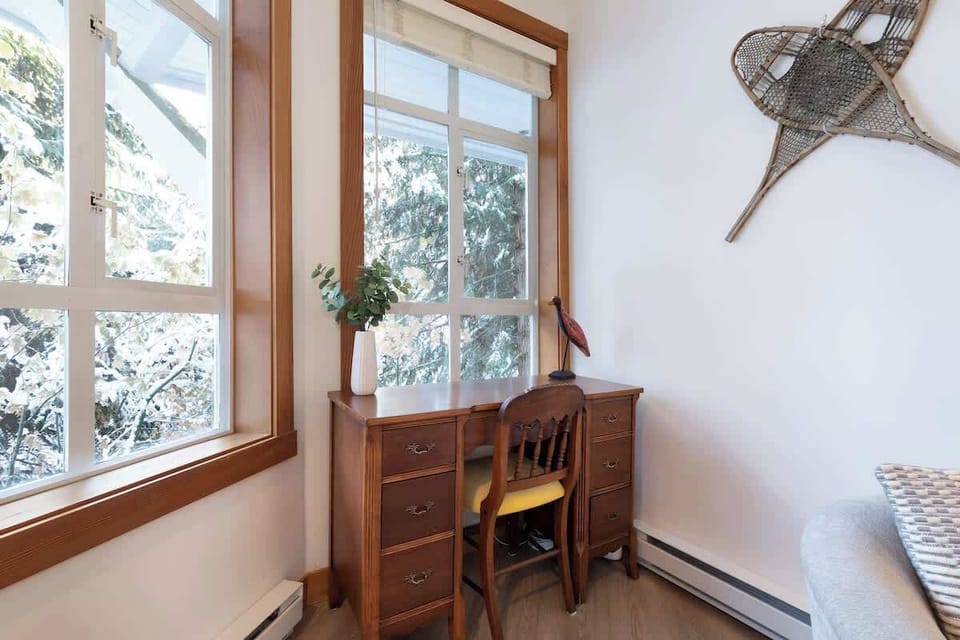 - Bright workspace by large windows offering peaceful snowy forest views  
- Wooden desk setup ideal for remote work or quiet moments in Whistler retreat  
- Natural light and alpine scenery create a calming productive corner  
