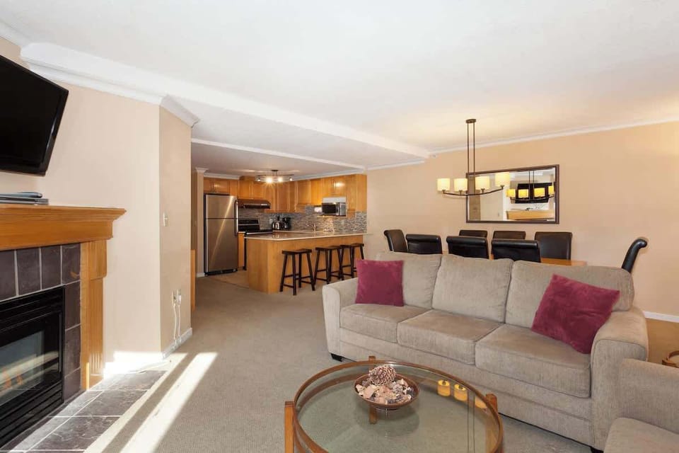 - Spacious living area with fireplace and mountain views for relaxing après-ski evenings  
- Comfortable seating with flat-screen TV and natural light filling the room  
- Open layout connecting living, dining, and kitchen for a warm mountain retreat