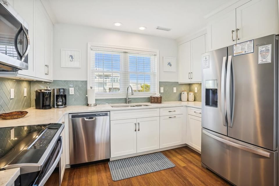 Your kitchen glows with natural light and coastal charm, featuring stainless steel appliances, custom backsplash, and ample prep space to create memorable vacation meals together.