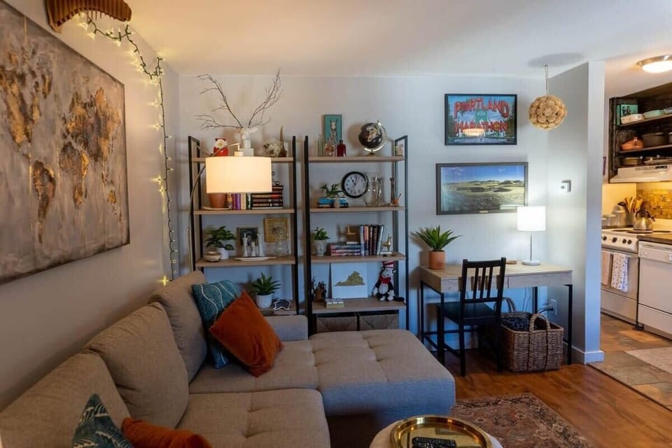 The cozy living room features a comfortable queen size sleeper sofa, a mounted flat-screen smart TV, bookshelves, a desk and chair, and an abundance of charming decor adding a homey ambiance to the space.