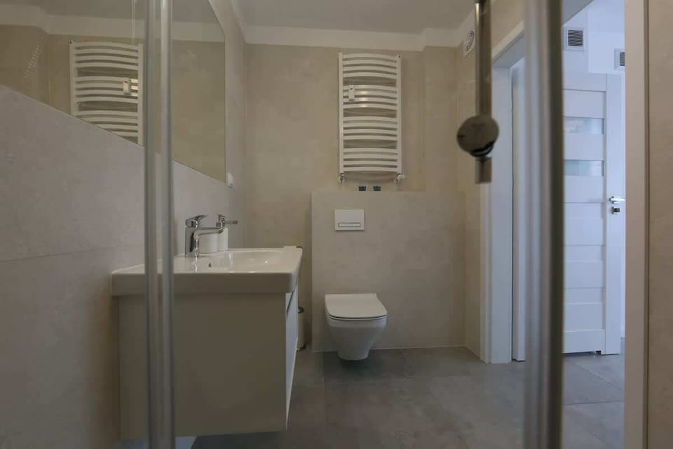 A compact bathroom featuring a glass-enclosed shower, a washing machine, and a white vanity, efficiently utilizing space.