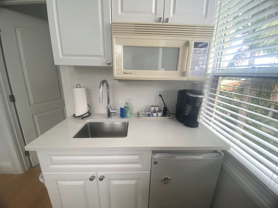 Kitchenette with microwave, mini fridge, Keurig coffee maker, glasses, plates, and cutlery. 