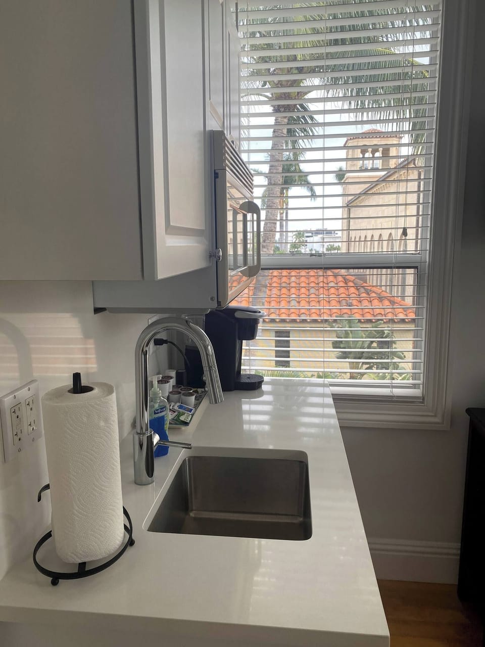 Kitchenette with microwave, mini fridge, Keurig coffee maker, glasses, plates, and cutlery. 