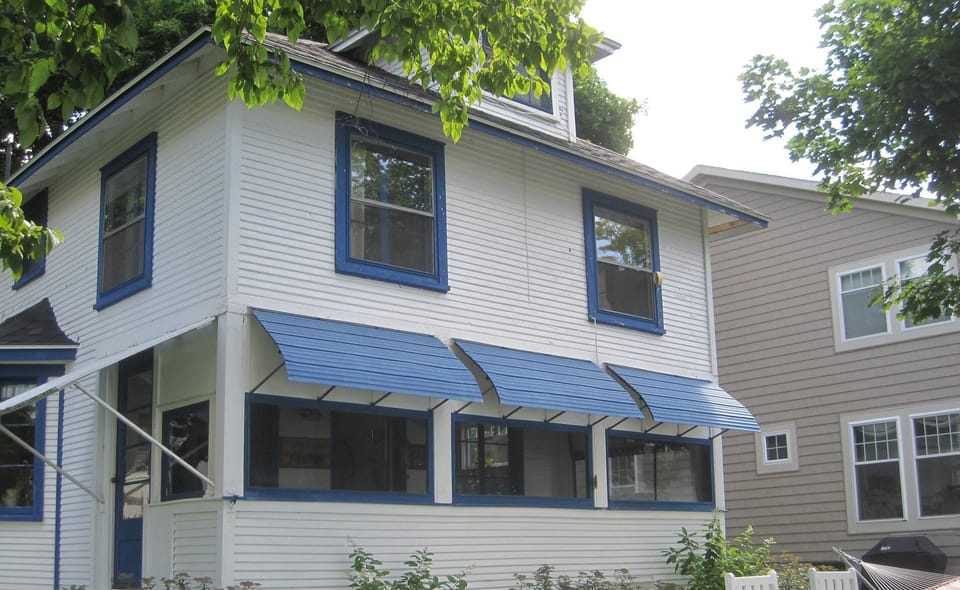 Bedrooms upstairs, porch downstairs, chairs, hammock, rockers on lakefront lawn.