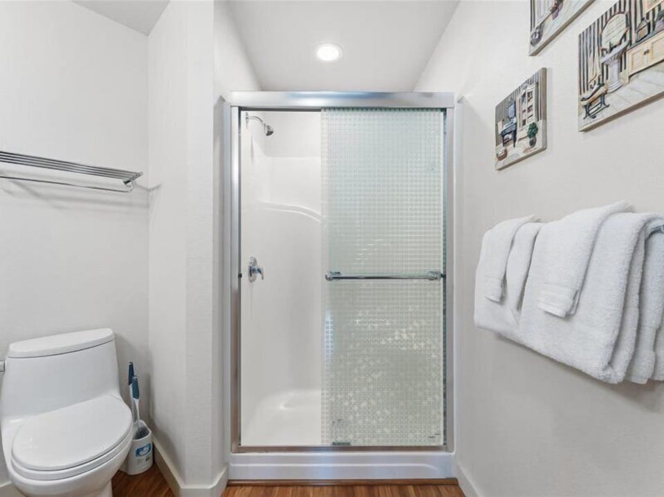 Step into your private bathroom, where crisp white fixtures and soft towels await. The walk-in shower invites you to refresh after a day of exploring, with warm wood flooring underfoot.