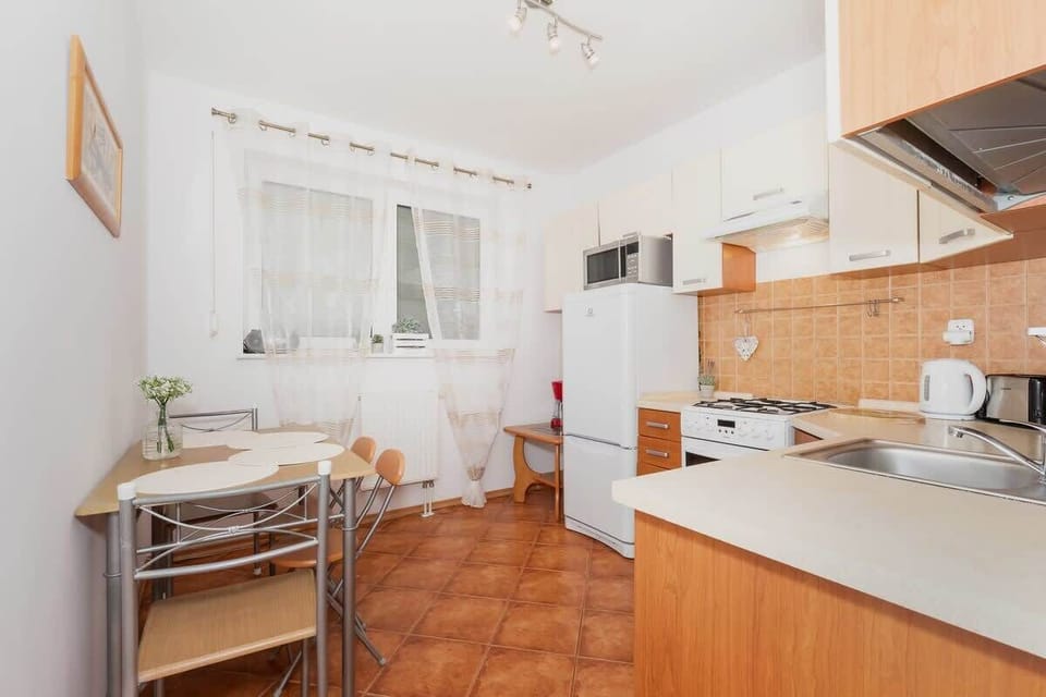 A bright kitchen with white cabinets and wooden countertops. The room has a window, adding natural light, and the floor has a warm-toned tile pattern.