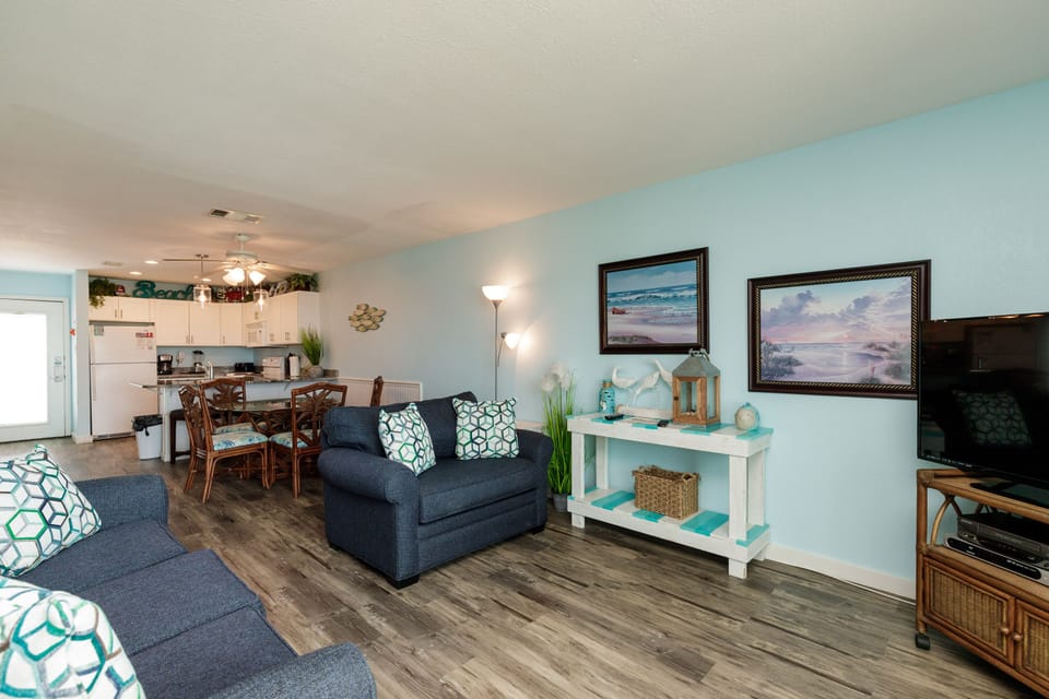 Relax in your coastal-themed living space featuring comfy navy sofas and beachside artwork that sets the perfect vacation mood.