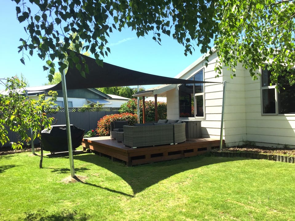 Outdoor seating area under shade cloth next to BBQ and in the back garden