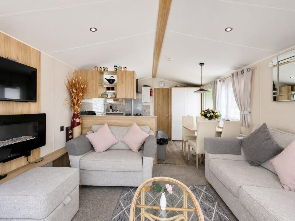 Light gray sofas with pastel cushions face a wall-mounted TV and electric fireplace in the living area.