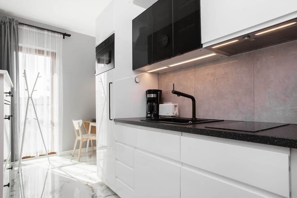 A compact kitchen with white cabinets, a black countertop, and integrated appliances, including a stovetop and kettle.