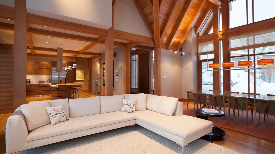 - Open-concept living area with vaulted ceilings and soft sectional seating  
- Natural wood beams and warm tones create a cozy mountain aesthetic  
- Perfect for family gatherings or relaxing by the fire after skiing  
