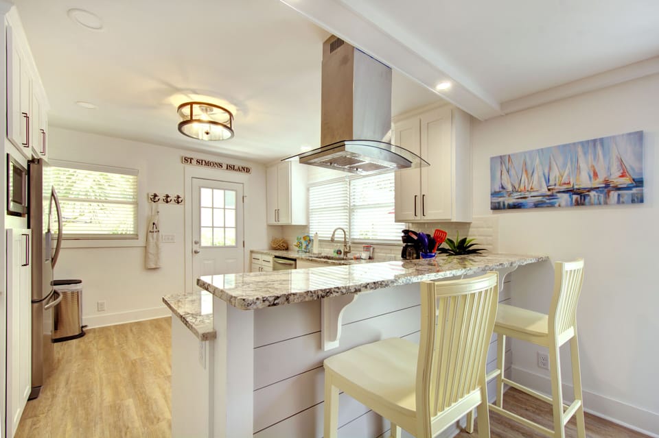 Kitchen Bar Seating And Open Layout - Bar stools at the island add casual seating beside the gas range, full fridge, and dining table.