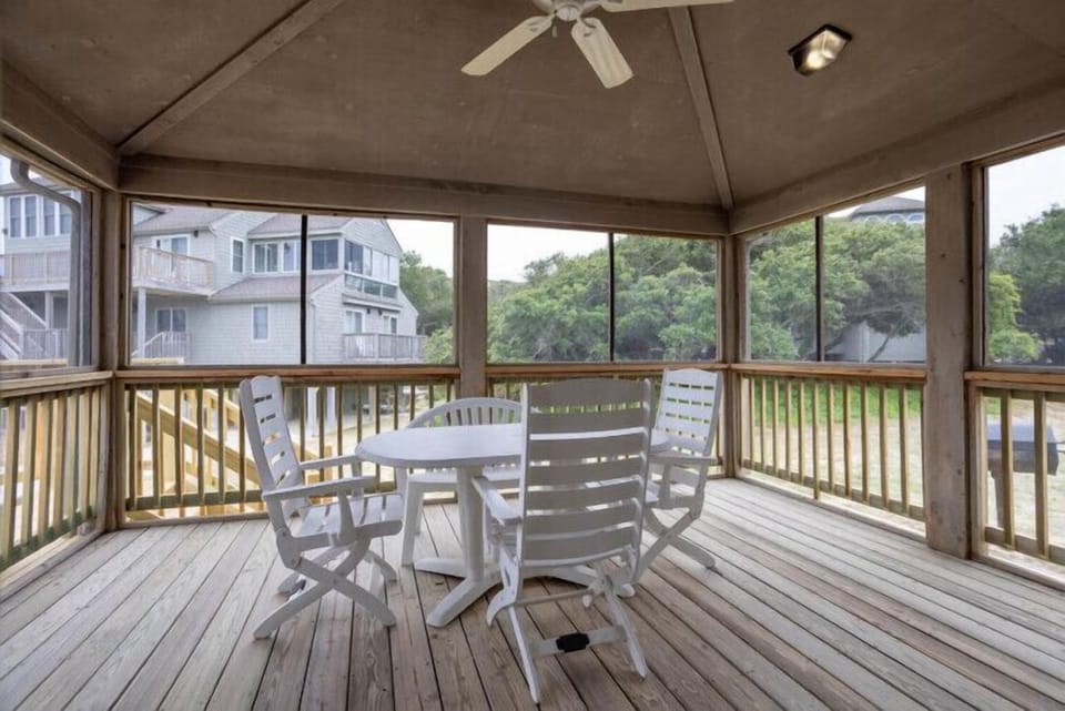 Sip your morning coffee in this screened porch, where coastal breezes drift through as you gaze out at lush greenery and neighboring beach homes—your peaceful spot between adventures.