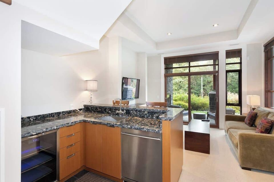 - Granite wet bar with wine fridge and modern design for entertaining  
- Overlooks a bright living area with large windows and forest views  
- Great space for mixing drinks and enjoying cozy nights in