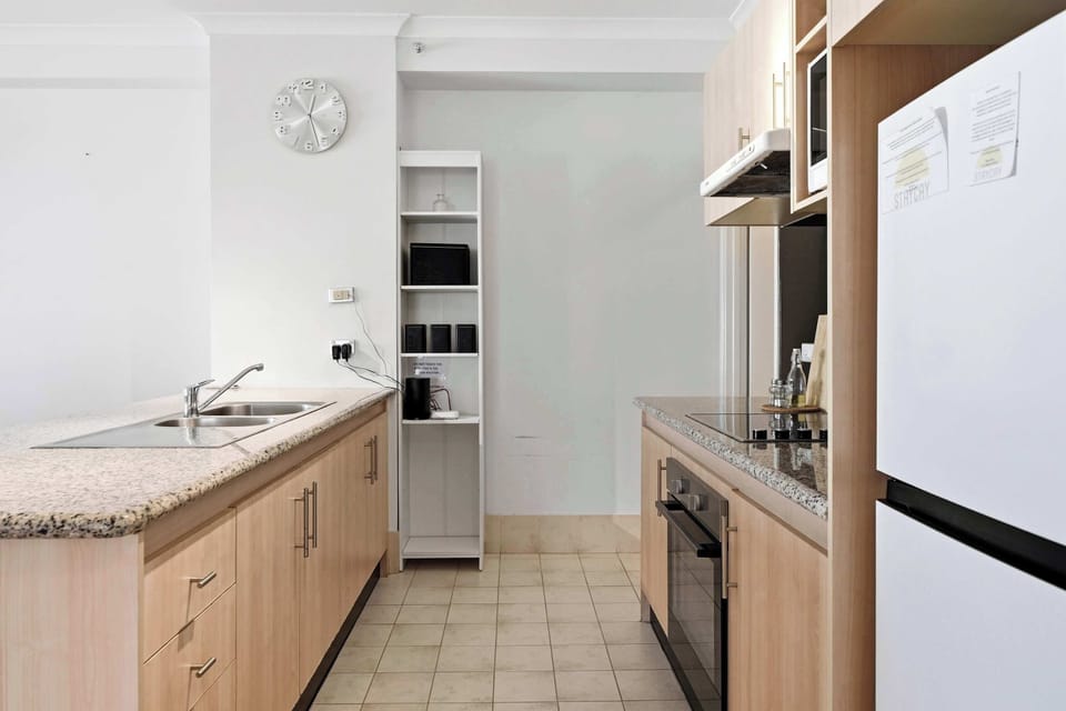 Bright & modern kitchen with granite countertops, full-size fridge, oven, stovetop, microwave, double sink, and spacious cabinetry. Featuring sleek wooden finishes, open shelving, and a clean minimalist design — perfect for short or long stays.
