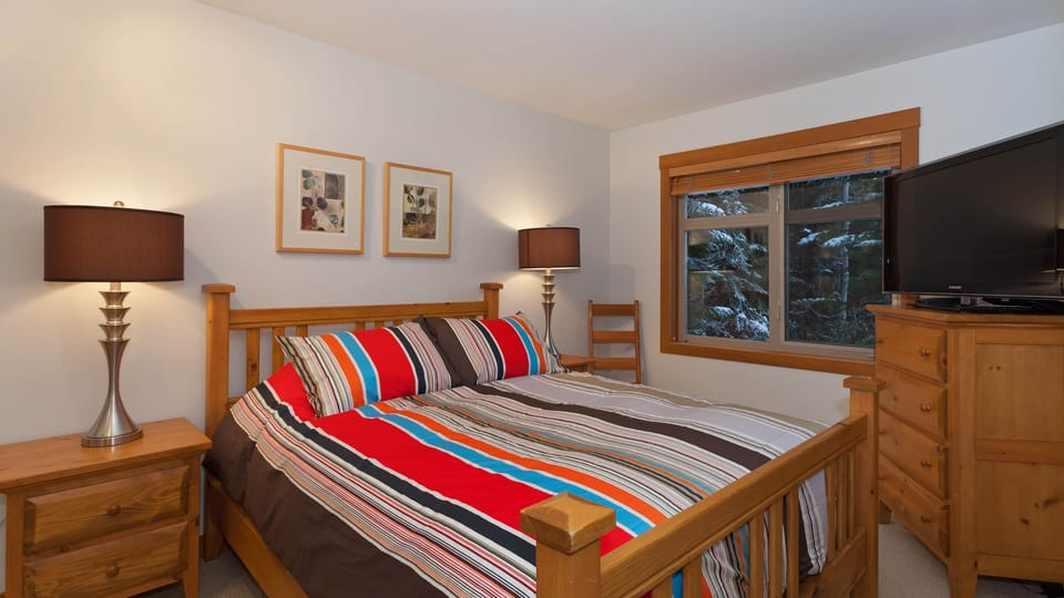 - Bedroom with vibrant striped bedding and cozy wooden furniture  
- Large window brings in peaceful forest views and soft daylight  
- A charming and inviting retreat for restful nights  
