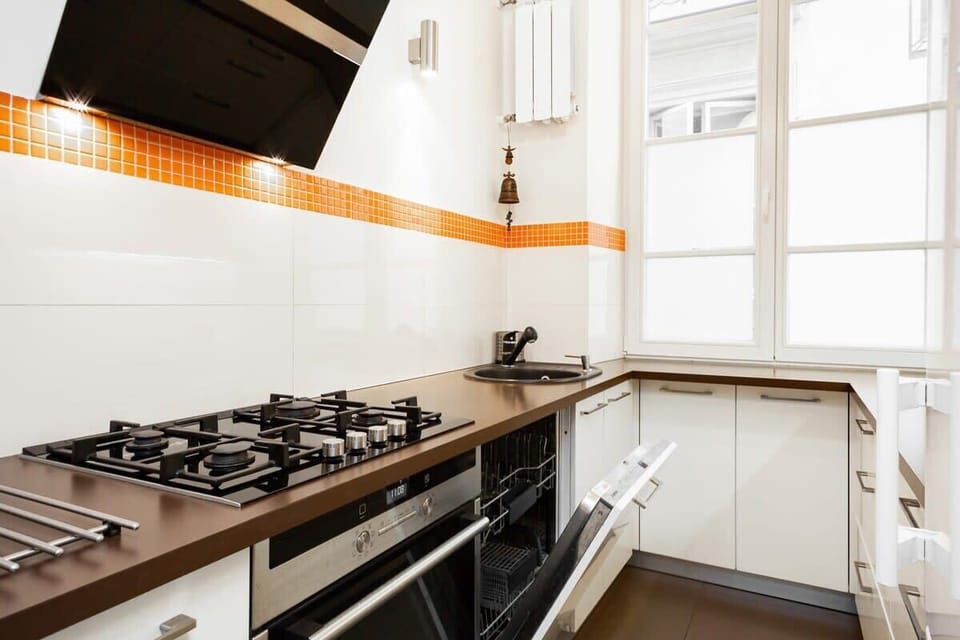 A small, modern kitchen with white cabinets, an orange accent strip, and a gas stove. The layout is efficient, maximizing counter space.