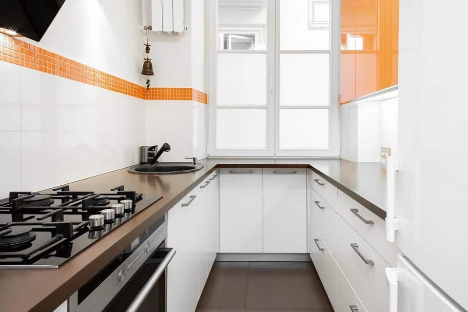 A close-up of a modern kitchen with a gas stove, white cabinets, and an orange accent line on the wall. The kitchen is sleek and functional.
