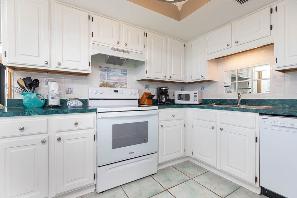 Inviting kitchen featuring white cabinetry and appliances, a vibrant turquoise countertop, and coffee maker