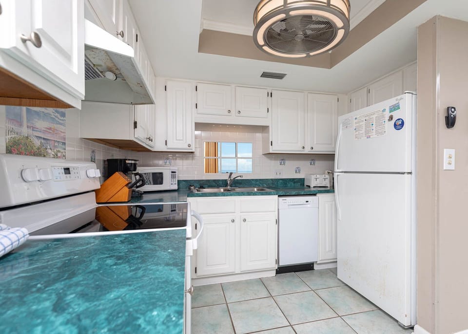 Bright kitchen featuring white cabinets, white appliances, and a sink mirror showcasing the lovely balcony view